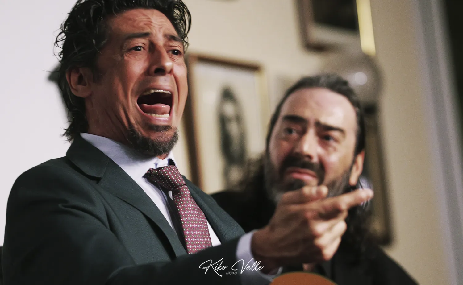 Man in a suit shouting with mouth open, while another man points or gestures beside him in a tense moment.
