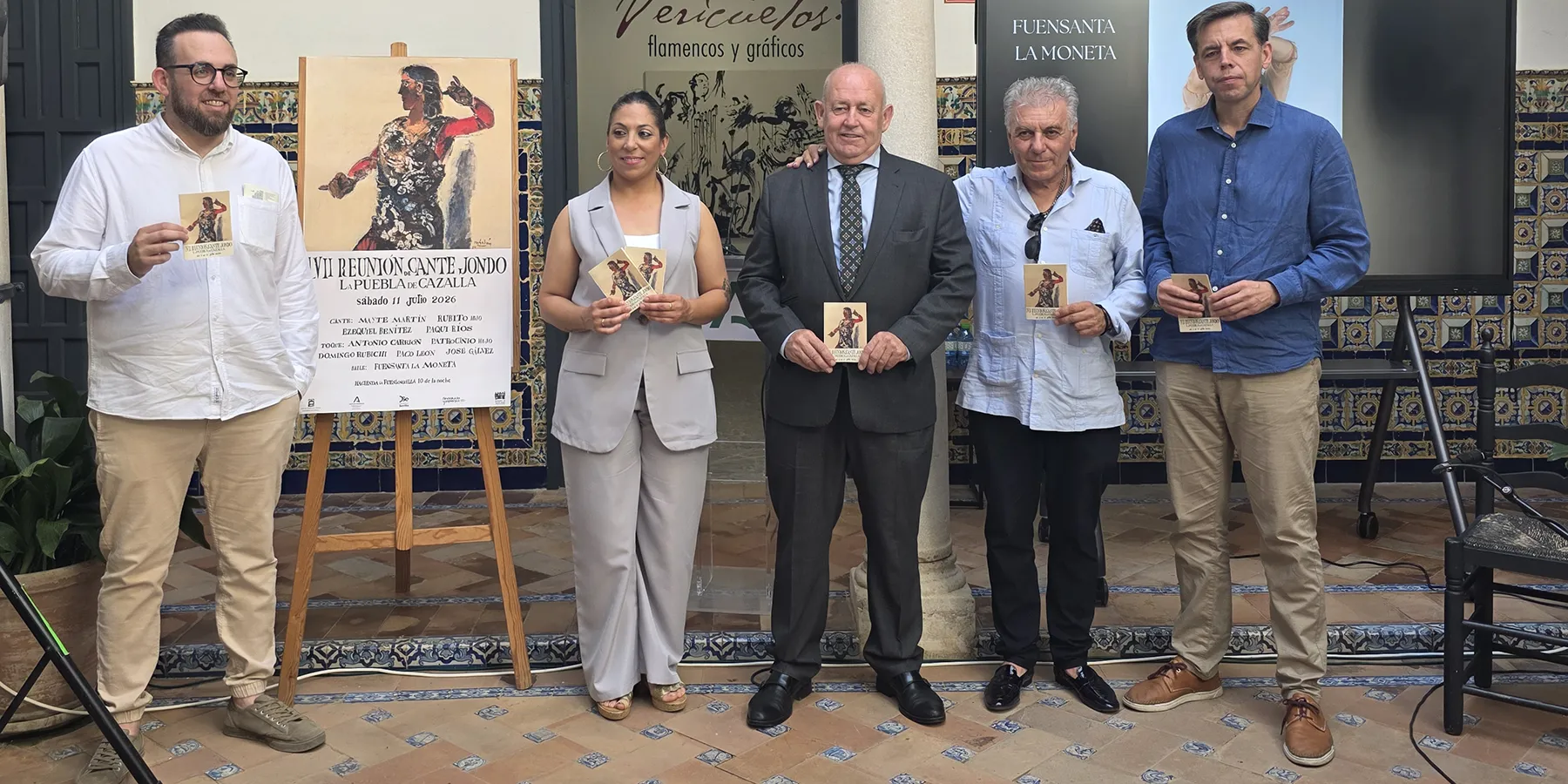 Five adults stand in a row, each holding event flyers, posing for a photo in front of a flamenco-themed poster and tiled backdrop.