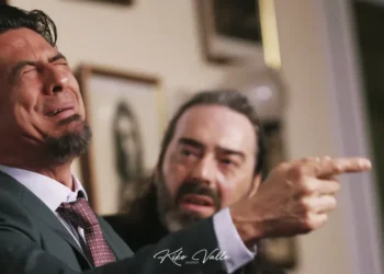Man in a suit cries in distress as another man with a beard points angrily indoors.
