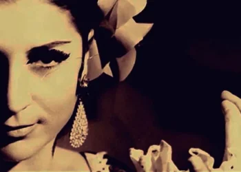 Vintage sepia portrait of a woman with a flower in her hair, dangling earrings, and a two-finger peace gesture near her face.