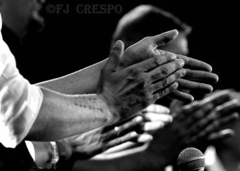 People clapping on stage with a microphone in the foreground in a black-and-white photo.