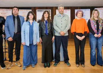 Eight adults pose for a group photo in a hall with flamenco event posters in the background.