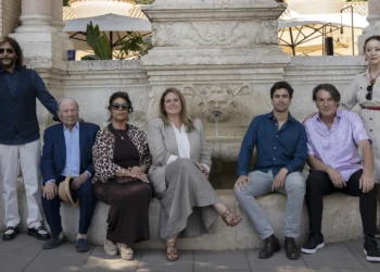Group of ten adults posing for a photo in front of a carved stone fountain on a sunny day.