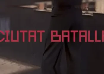 Wall with red text 'CIUTAT BATALLA' in bold letters, person walking by in dark clothing (informative).