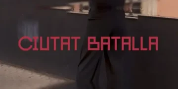 Wall with red text 'CIUTAT BATALLA' in bold letters, person walking by in dark clothing (informative).