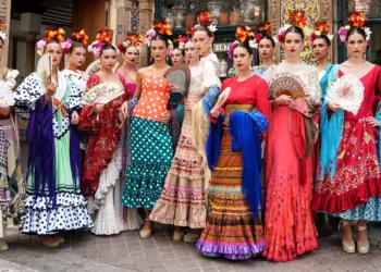 Group of women in vibrant flamenco dresses with flowers in hair, posing on a decorative street.
